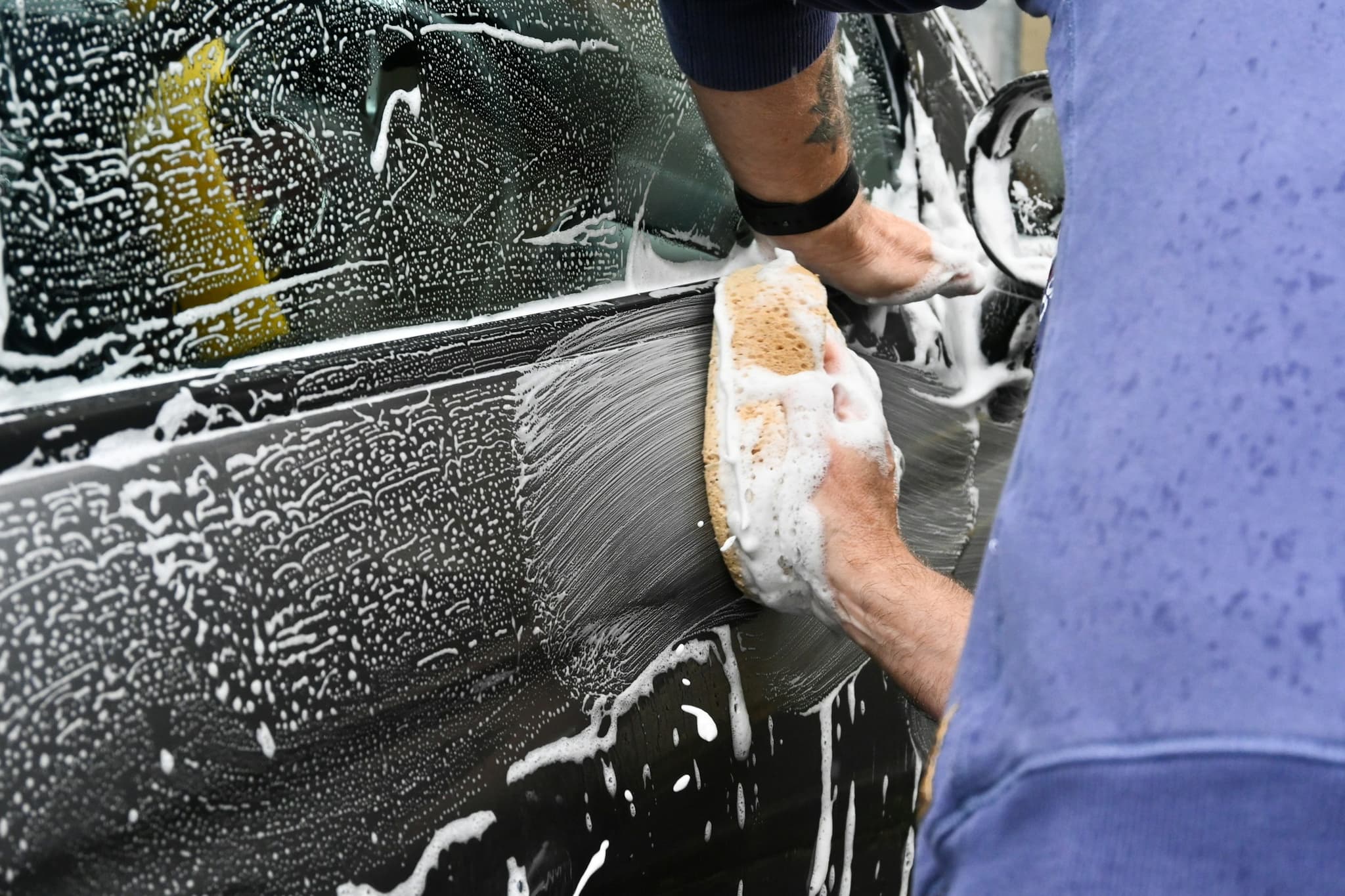A car being washed by hand with a soapy sponge