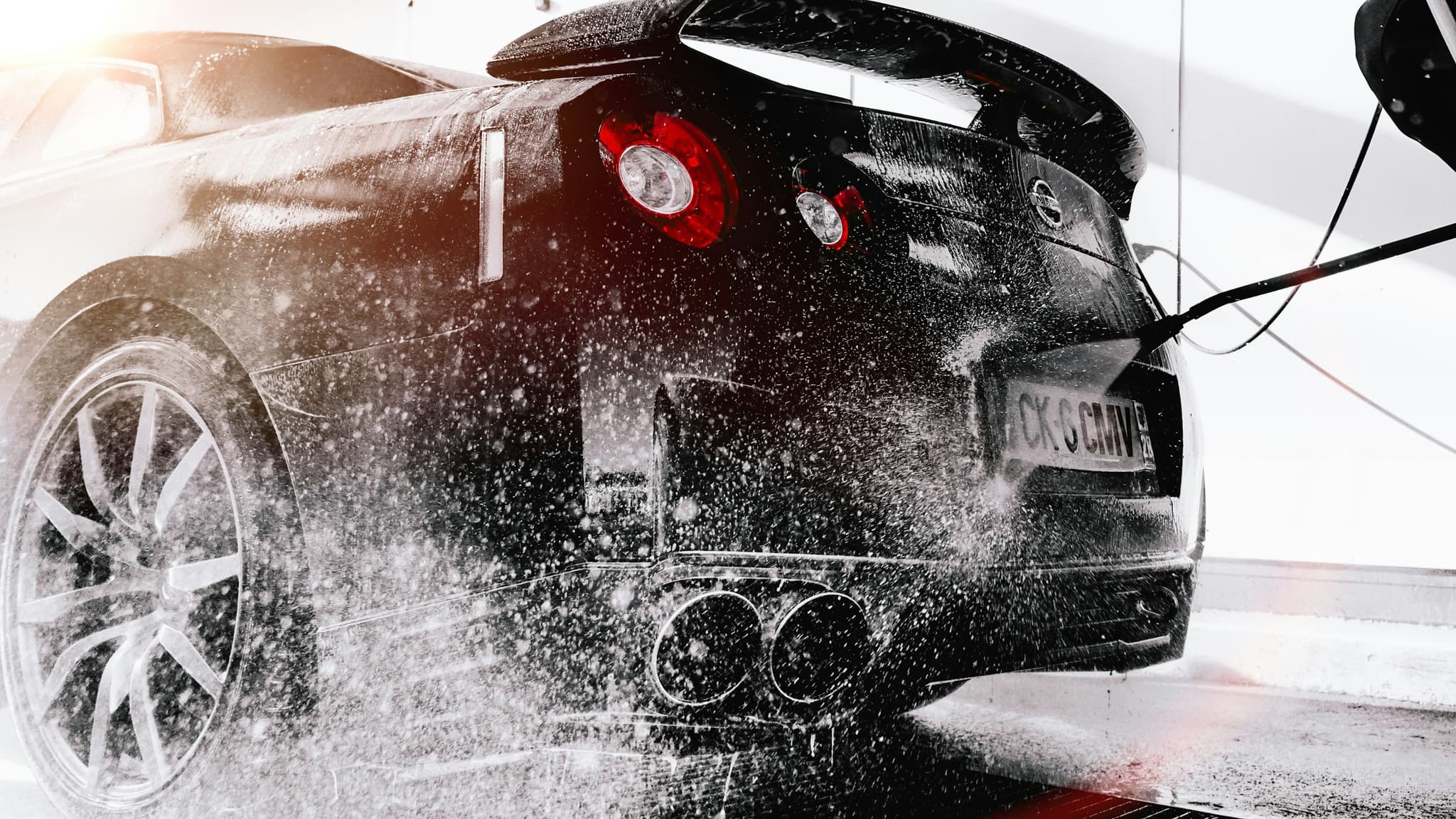 Water spraying across the rear of a sports car during a wash